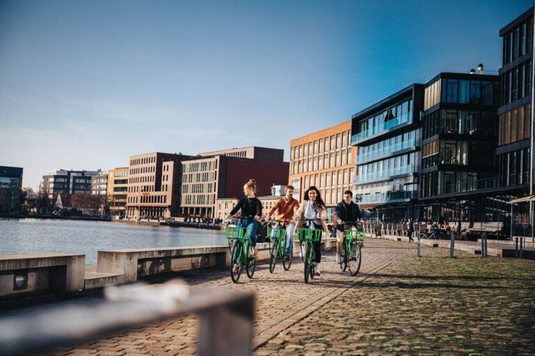 Fyra unga personer cyklar glatt längs vattnet i en stad
