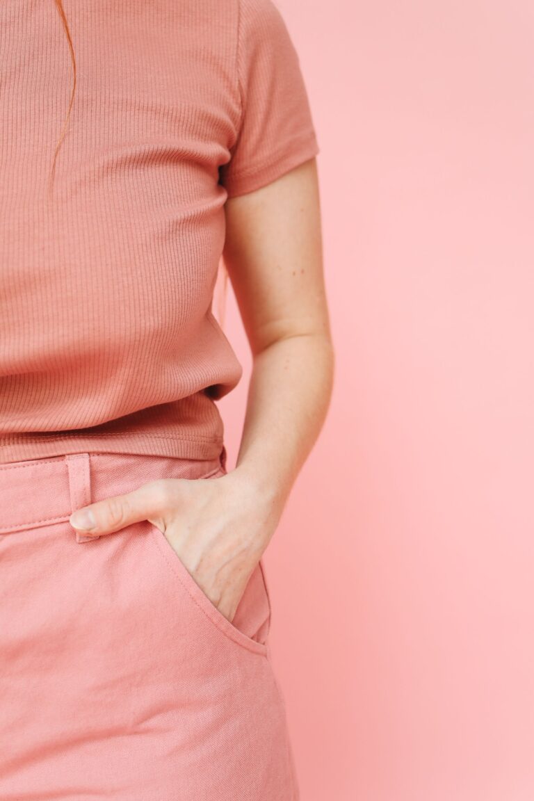 En kvinna i rosa kläder med handen i fickan mot ljusrosa bakgrund