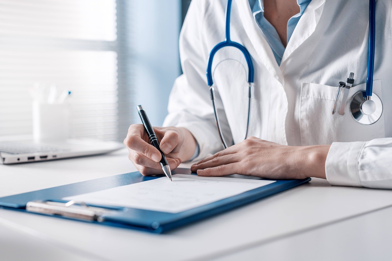 Läkare i vit rock med stetoskop skriver på en patients journal