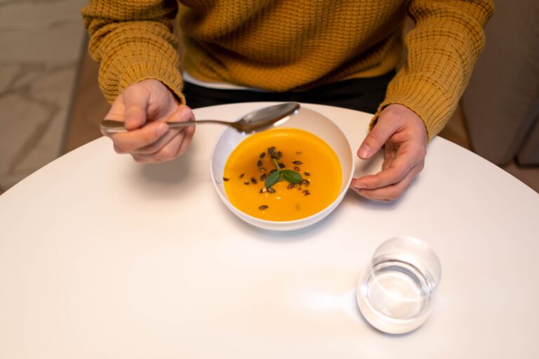 En person i gul tröja äter en skål med orange pumpasoppa med frön