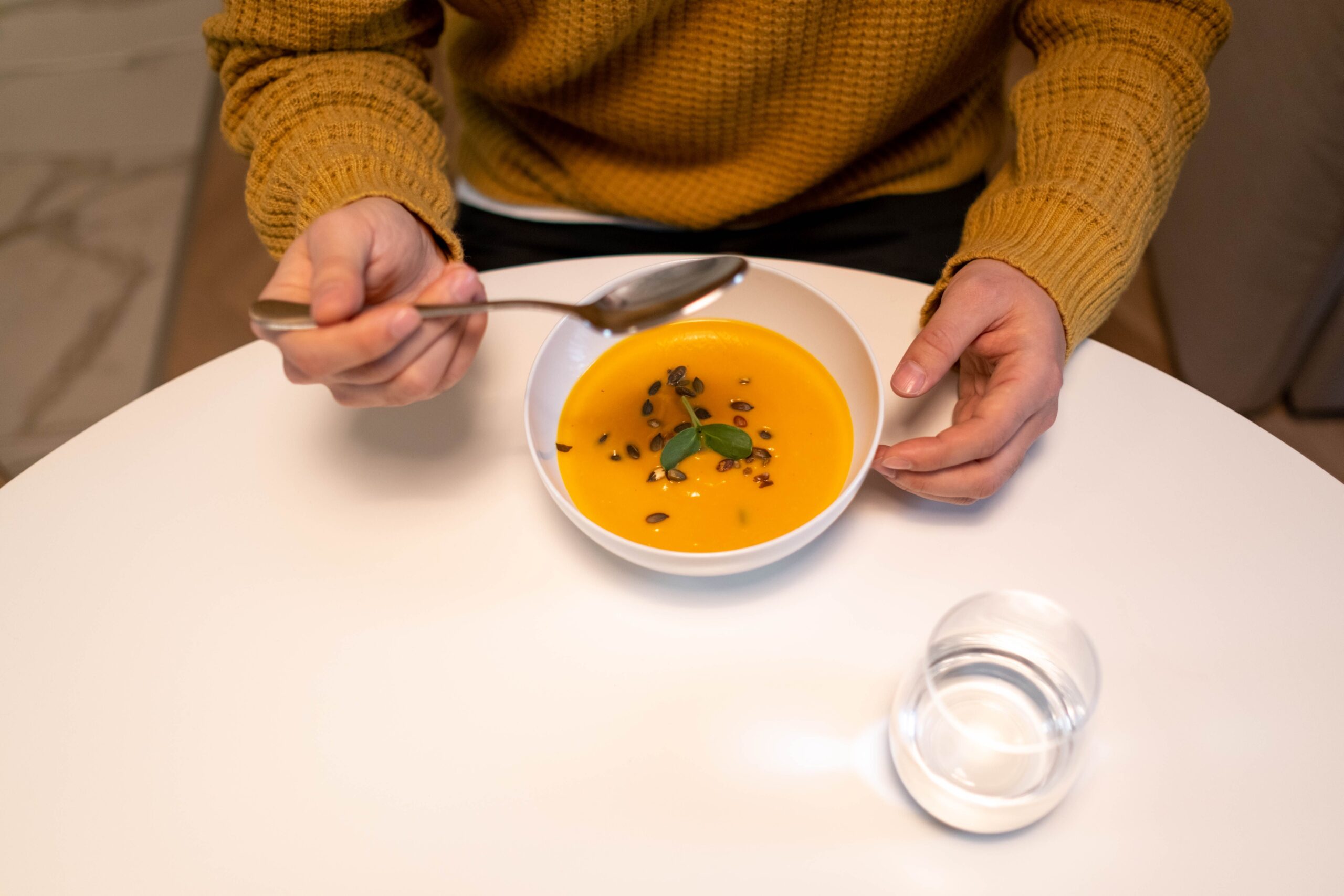 En person i gul tröja äter en skål med orange pumpasoppa med frön
