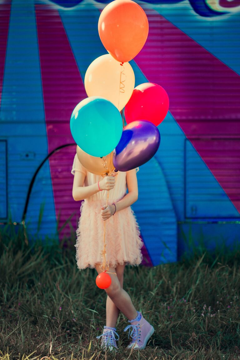 En tonåring håller i en stor bukett färgglada ballonger på en somrig gräsyta