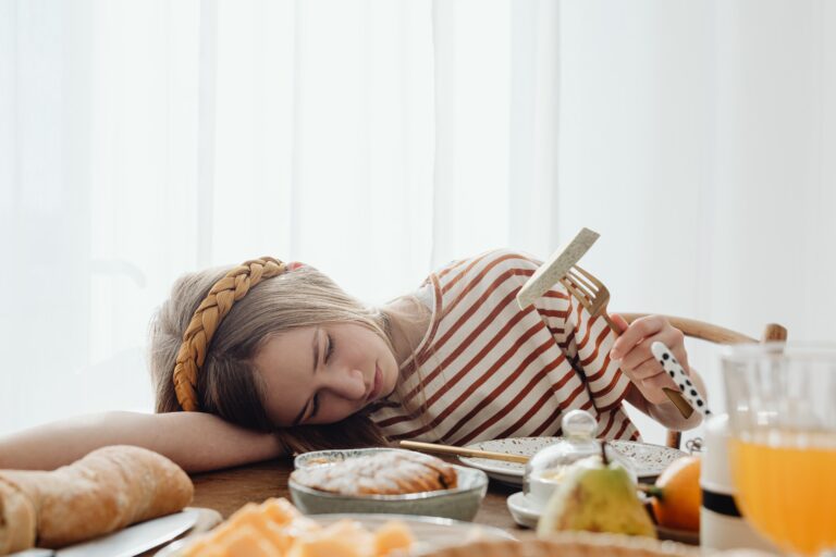 Trött flicka med flätat hårband vilar huvudet på bordet vid frukosten