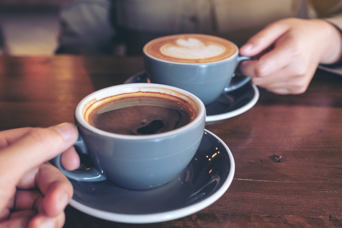 Två personer håller varsin grå kopp med kaffe på ett träbord